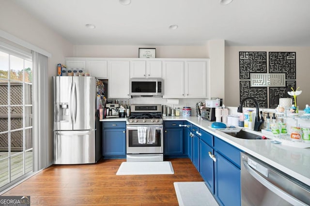 kitchen with white cabinets, blue cabinets, sink, hardwood / wood-style flooring, and appliances with stainless steel finishes