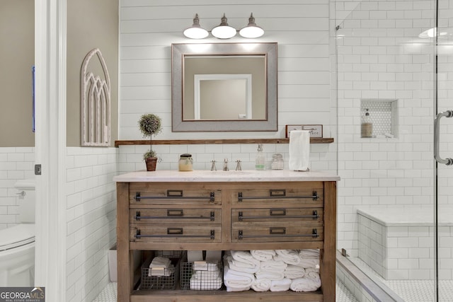 bathroom with vanity, a shower with shower door, tile walls, and toilet