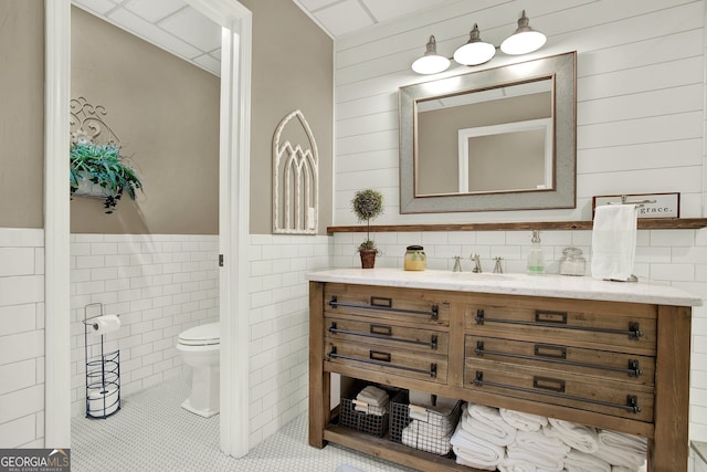 bathroom with tile patterned flooring, vanity, toilet, and tile walls