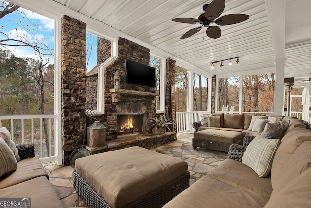 sunroom / solarium featuring ceiling fan, an outdoor stone fireplace, and track lighting