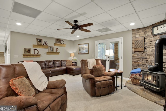 living room featuring a wood stove, a paneled ceiling, ceiling fan, and light colored carpet