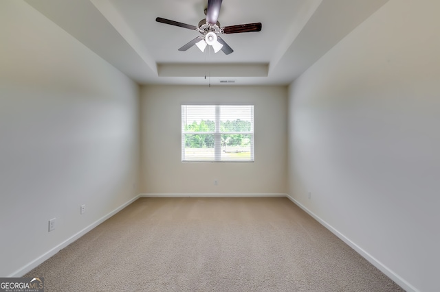 carpeted spare room featuring a tray ceiling and ceiling fan