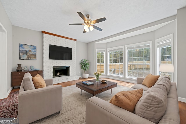 living room featuring a brick fireplace, ceiling fan, a textured ceiling, and light hardwood / wood-style flooring