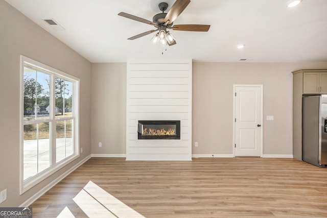 unfurnished living room with a large fireplace, light hardwood / wood-style flooring, and ceiling fan