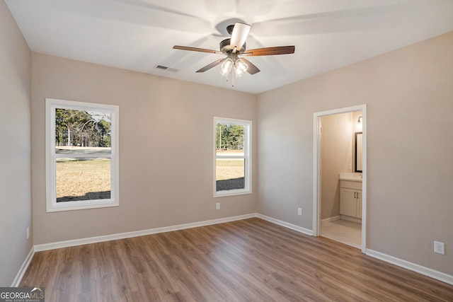 unfurnished bedroom with ceiling fan, light wood-type flooring, connected bathroom, and multiple windows