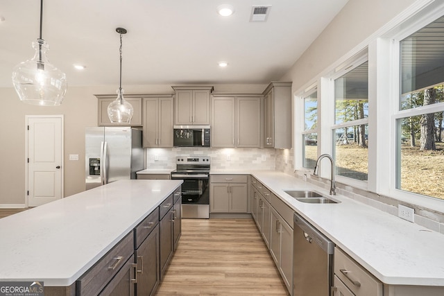 kitchen with tasteful backsplash, stainless steel appliances, sink, a kitchen island, and hanging light fixtures