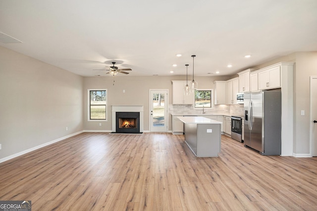 kitchen featuring white cabinetry, appliances with stainless steel finishes, decorative light fixtures, a kitchen island, and light wood-type flooring