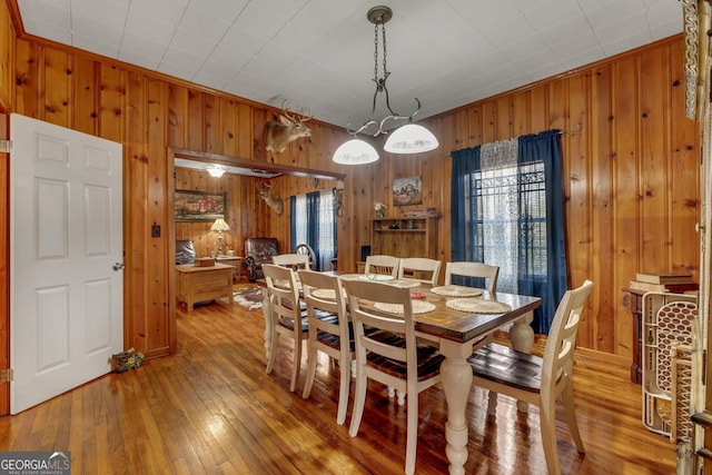 dining space featuring wood walls, crown molding, a healthy amount of sunlight, and hardwood / wood-style flooring