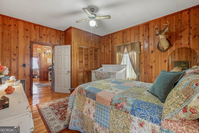 bedroom featuring crown molding, wooden walls, ceiling fan, light wood-type flooring, and a closet