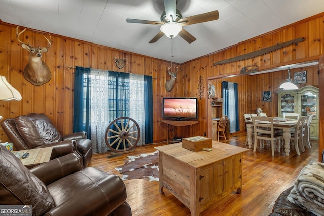 living room featuring ceiling fan, light wood-type flooring, crown molding, and wooden walls