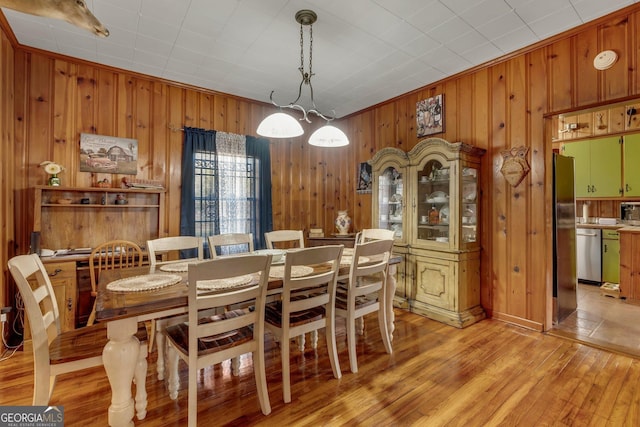 dining space featuring light wood-type flooring, ornamental molding, and wooden walls