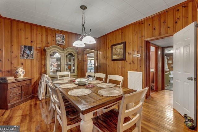 dining area with light wood-type flooring, crown molding, and wooden walls