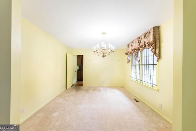 carpeted empty room featuring an inviting chandelier