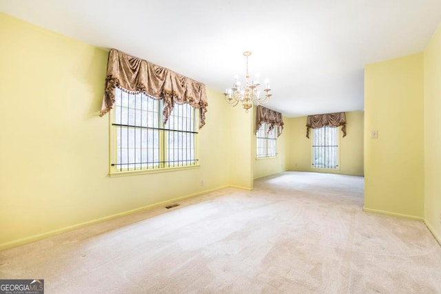 spare room featuring a chandelier, light colored carpet, and a wealth of natural light