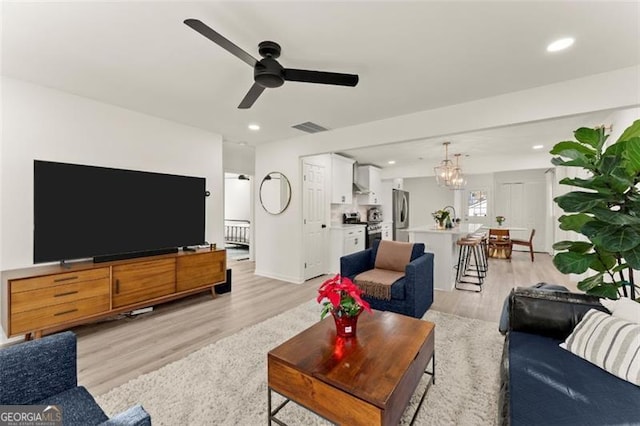 living room with ceiling fan with notable chandelier and light wood-type flooring