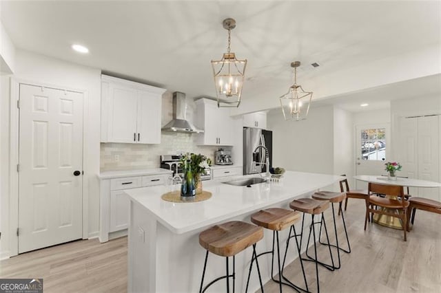 kitchen with wall chimney exhaust hood, stainless steel appliances, light hardwood / wood-style flooring, pendant lighting, and white cabinets