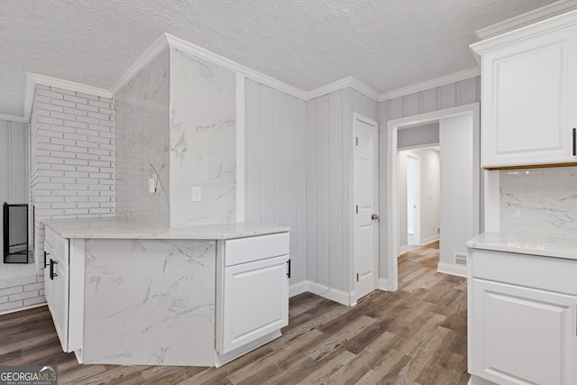 kitchen featuring white cabinets, hardwood / wood-style floors, a textured ceiling, and ornamental molding