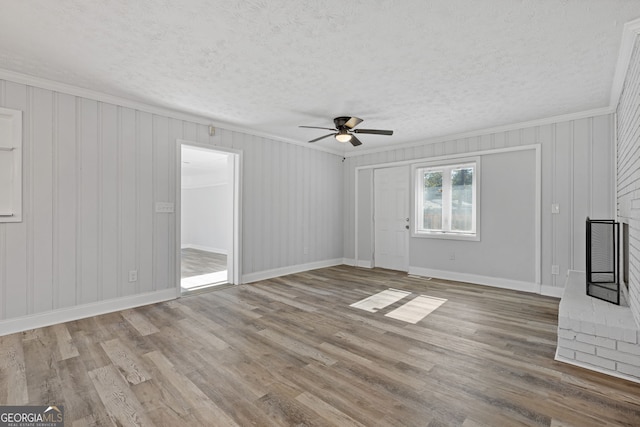 unfurnished living room with ornamental molding, a textured ceiling, ceiling fan, hardwood / wood-style floors, and wood walls