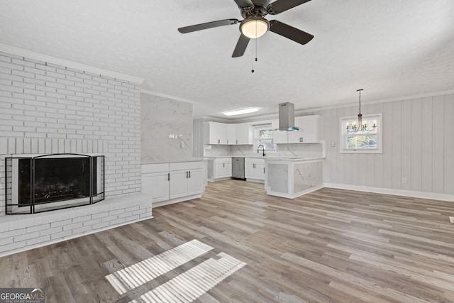 unfurnished living room featuring a brick fireplace, ornamental molding, ceiling fan with notable chandelier, a textured ceiling, and light hardwood / wood-style flooring