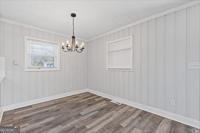 empty room featuring hardwood / wood-style floors, crown molding, wooden walls, and a chandelier