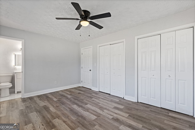 unfurnished bedroom with connected bathroom, ceiling fan, hardwood / wood-style floors, a textured ceiling, and two closets