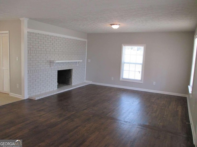 unfurnished living room featuring dark hardwood / wood-style flooring, a textured ceiling, and a brick fireplace