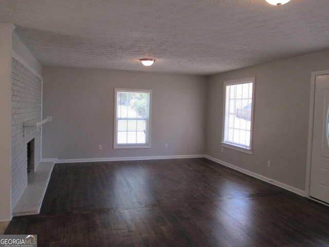 unfurnished living room featuring a wealth of natural light, a fireplace, dark wood-type flooring, and a textured ceiling