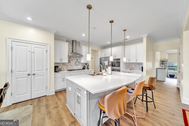 kitchen featuring a breakfast bar, a center island with sink, white cabinets, and wall chimney range hood