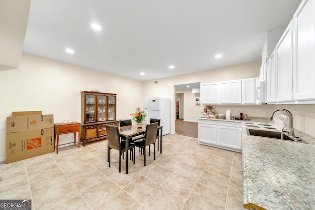 kitchen with light stone countertops, white appliances, sink, light tile patterned floors, and white cabinetry