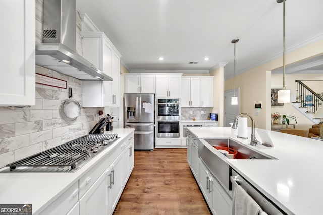 kitchen featuring pendant lighting, backsplash, white cabinets, wall chimney exhaust hood, and appliances with stainless steel finishes