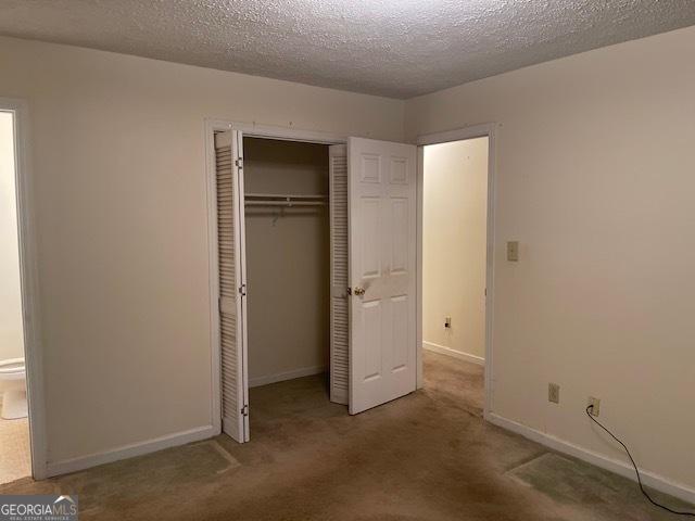 unfurnished bedroom featuring carpet floors, a textured ceiling, and a closet