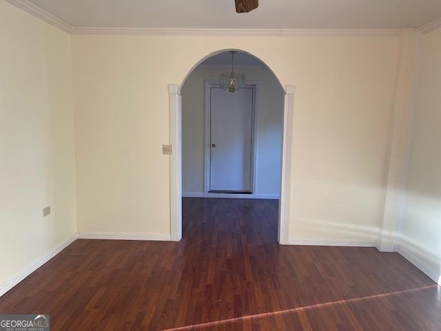 spare room featuring dark hardwood / wood-style flooring, a notable chandelier, and ornamental molding