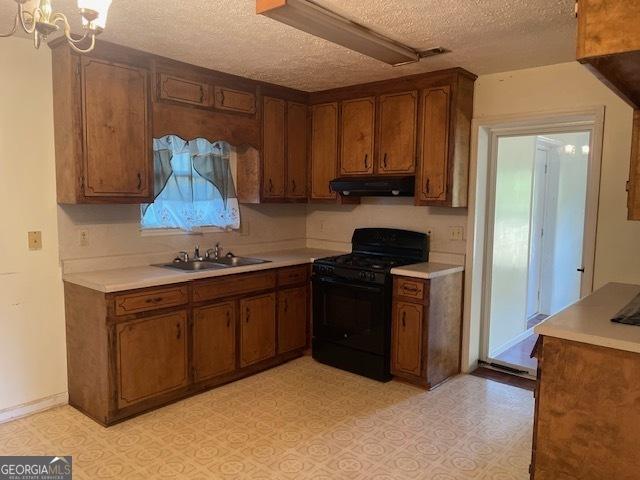 kitchen with a textured ceiling, gas stove, sink, and an inviting chandelier