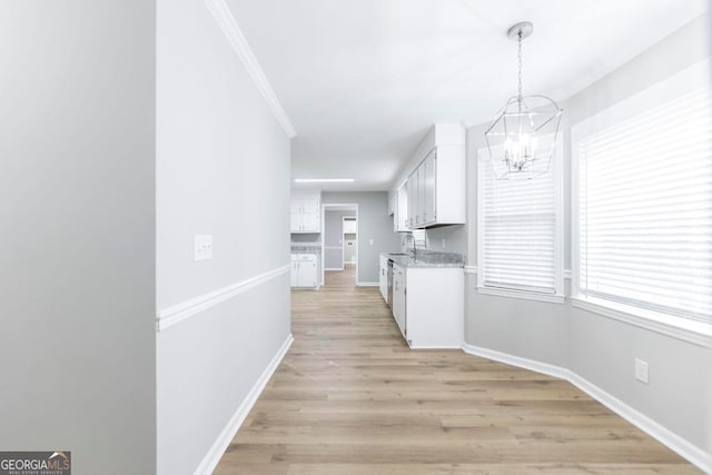 kitchen with white cabinets, light hardwood / wood-style flooring, hanging light fixtures, and ornamental molding