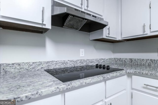 kitchen featuring light stone counters, black electric stovetop, and white cabinets