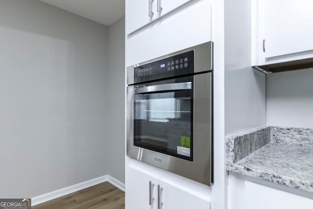 kitchen featuring white cabinets, dark hardwood / wood-style flooring, light stone countertops, and stainless steel oven