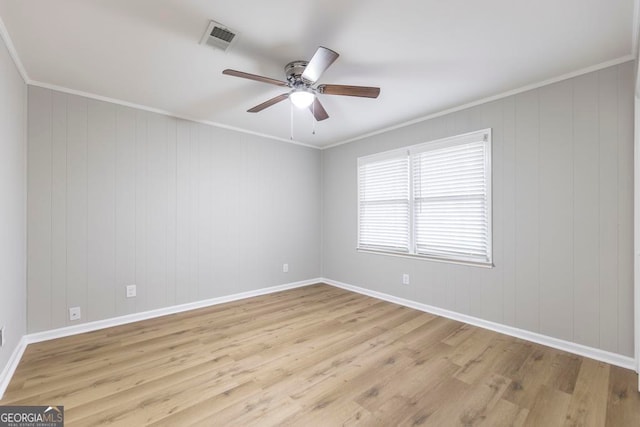 empty room with ceiling fan, light wood-type flooring, ornamental molding, and wooden walls