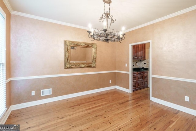 unfurnished dining area featuring hardwood / wood-style flooring, an inviting chandelier, a wealth of natural light, and crown molding