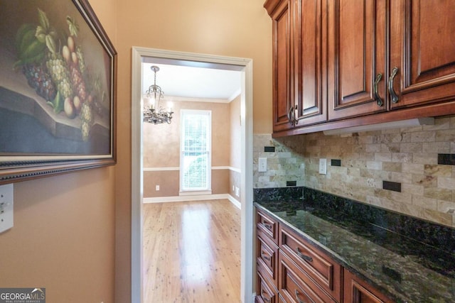 kitchen with dark stone counters, crown molding, light hardwood / wood-style flooring, decorative backsplash, and a chandelier