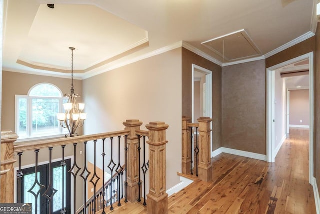 corridor with a chandelier, hardwood / wood-style flooring, a raised ceiling, and ornamental molding