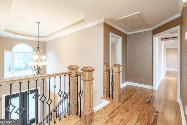 hallway featuring a chandelier, light hardwood / wood-style floors, a raised ceiling, and ornamental molding