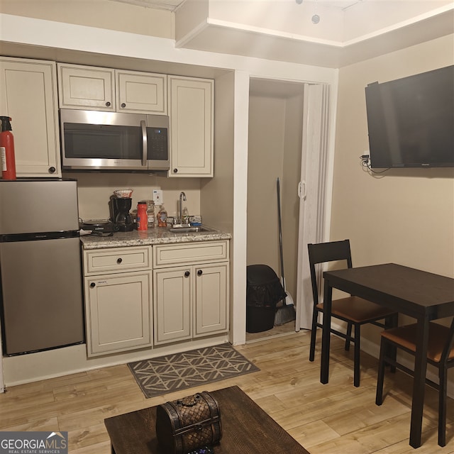 kitchen with light wood-type flooring, stainless steel appliances, light stone counters, and sink