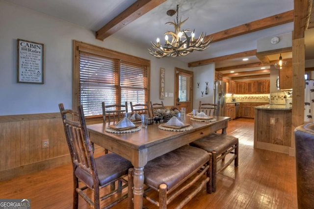 dining space with a chandelier, beam ceiling, light hardwood / wood-style flooring, and wooden walls