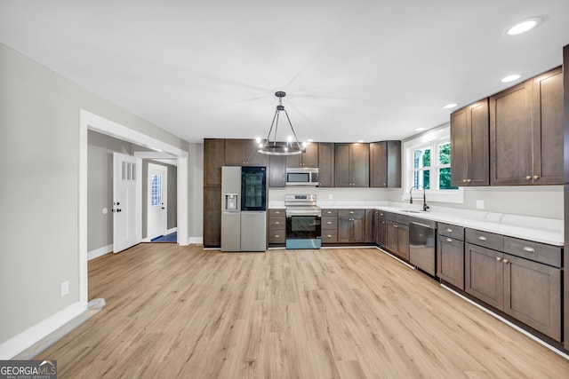 kitchen with sink, dark brown cabinets, hanging light fixtures, light wood-type flooring, and stainless steel appliances