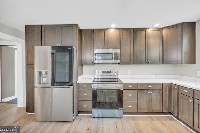 kitchen featuring dark brown cabinetry, appliances with stainless steel finishes, light stone countertops, and light hardwood / wood-style floors