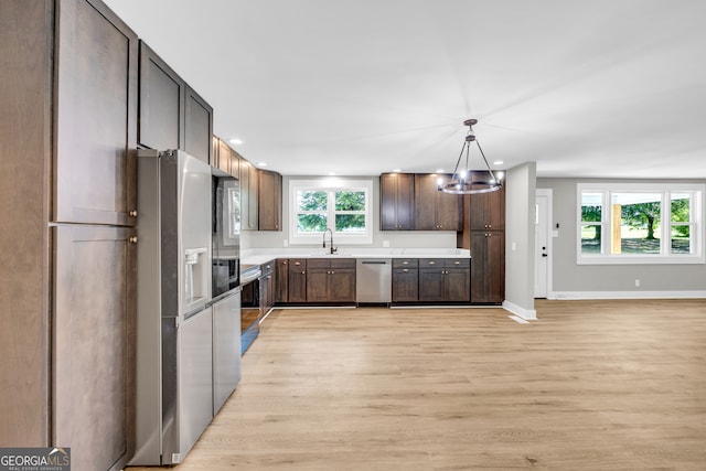 kitchen with sink, dark brown cabinets, hanging light fixtures, light wood-type flooring, and stainless steel appliances