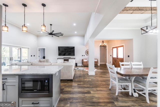 kitchen with light stone countertops, ceiling fan with notable chandelier, built in microwave, dark wood-type flooring, and hanging light fixtures