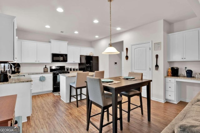 kitchen featuring pendant lighting, a center island, black appliances, white cabinets, and light hardwood / wood-style floors