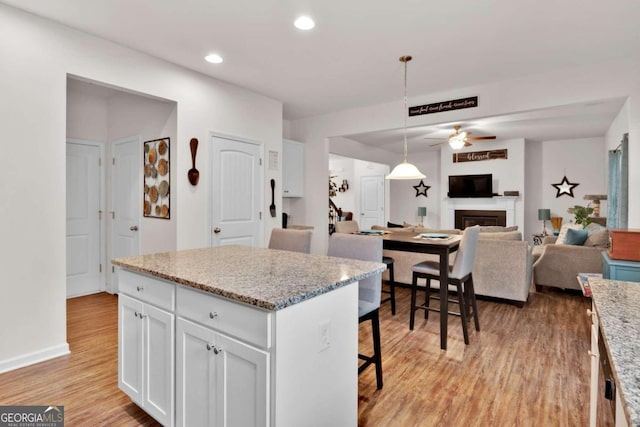 kitchen with a center island, hanging light fixtures, light hardwood / wood-style flooring, ceiling fan, and white cabinetry