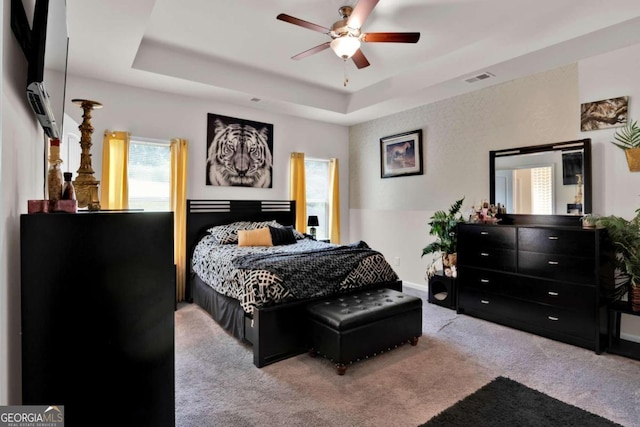 bedroom with light colored carpet, a raised ceiling, and ceiling fan